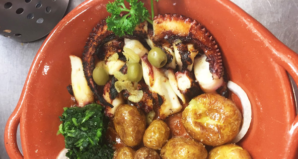 Plat de poulpe grillé accompagné de pommes de terre, servi dans un plat en terre cuite